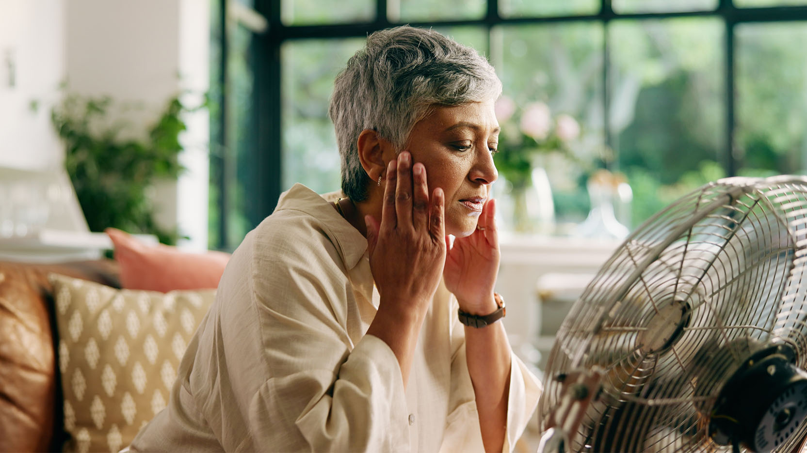 Older woman sits in front of electric fan to cool off