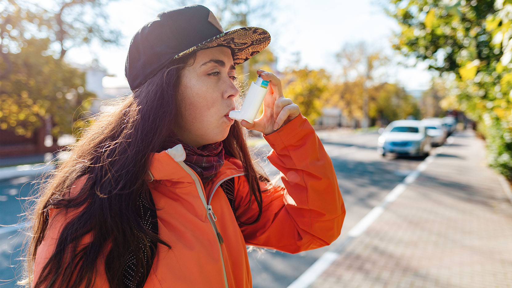 A young woman walking outdoors using an asthma inhaler