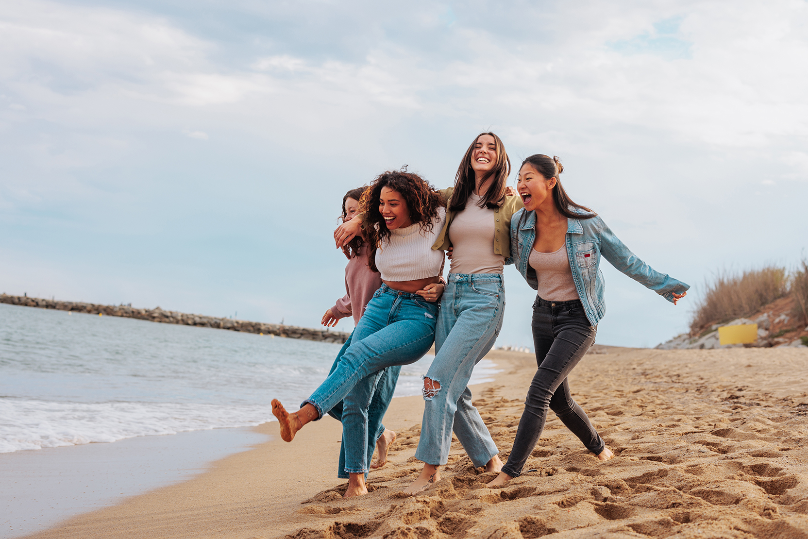 Four young women laughing together as they walk on a beach