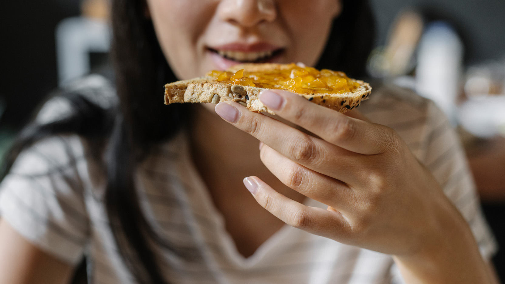 An anonymous young woman sitting at the dining table and enjoying her breakfast.