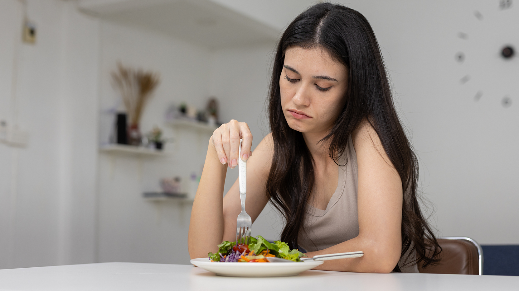Young woman looks upset while picking at a salad.