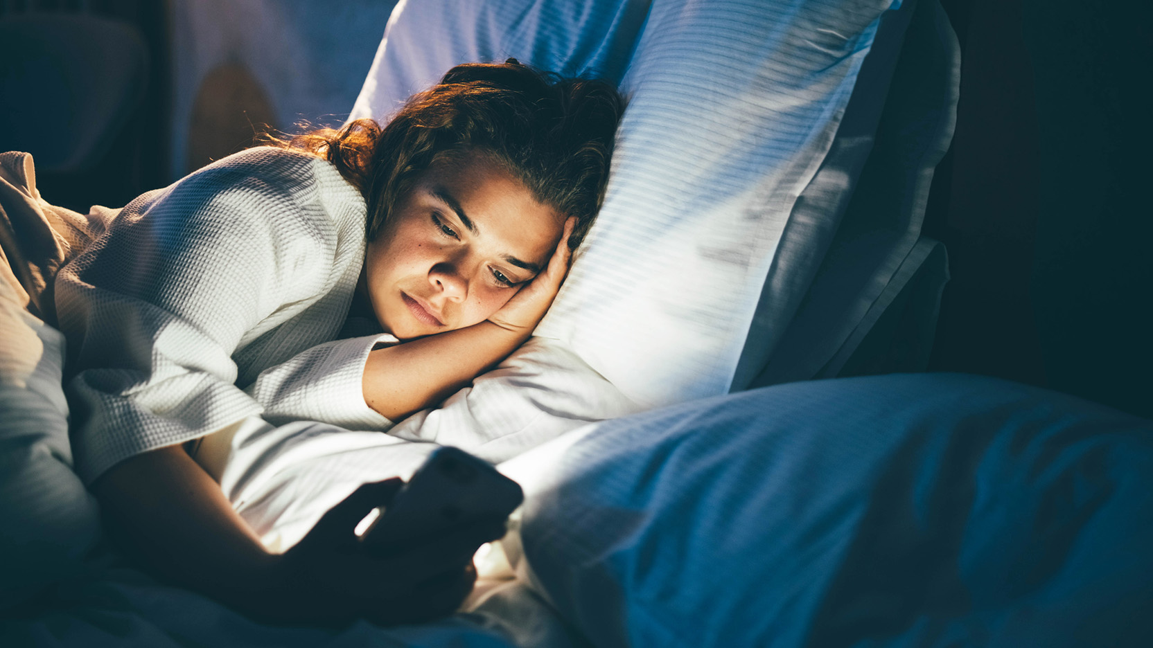 Young woman laying in bed and using smart phone.