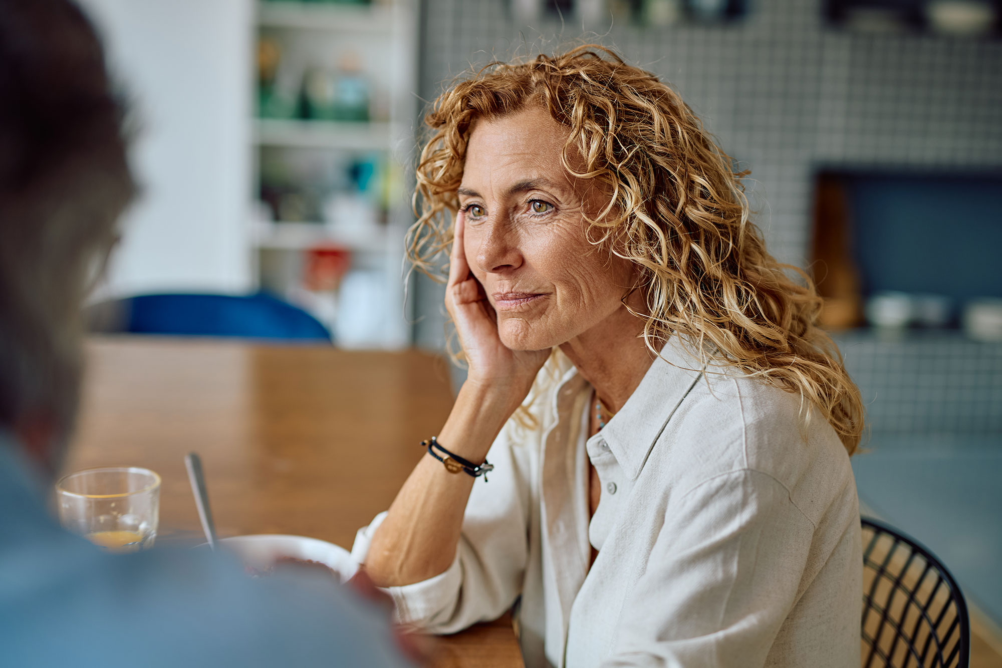 An older woman sits at a kitchen table chatting with someone 