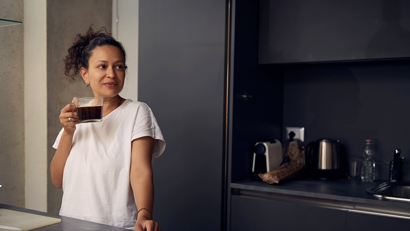 Woman standing in her kitchen drinking coffee
