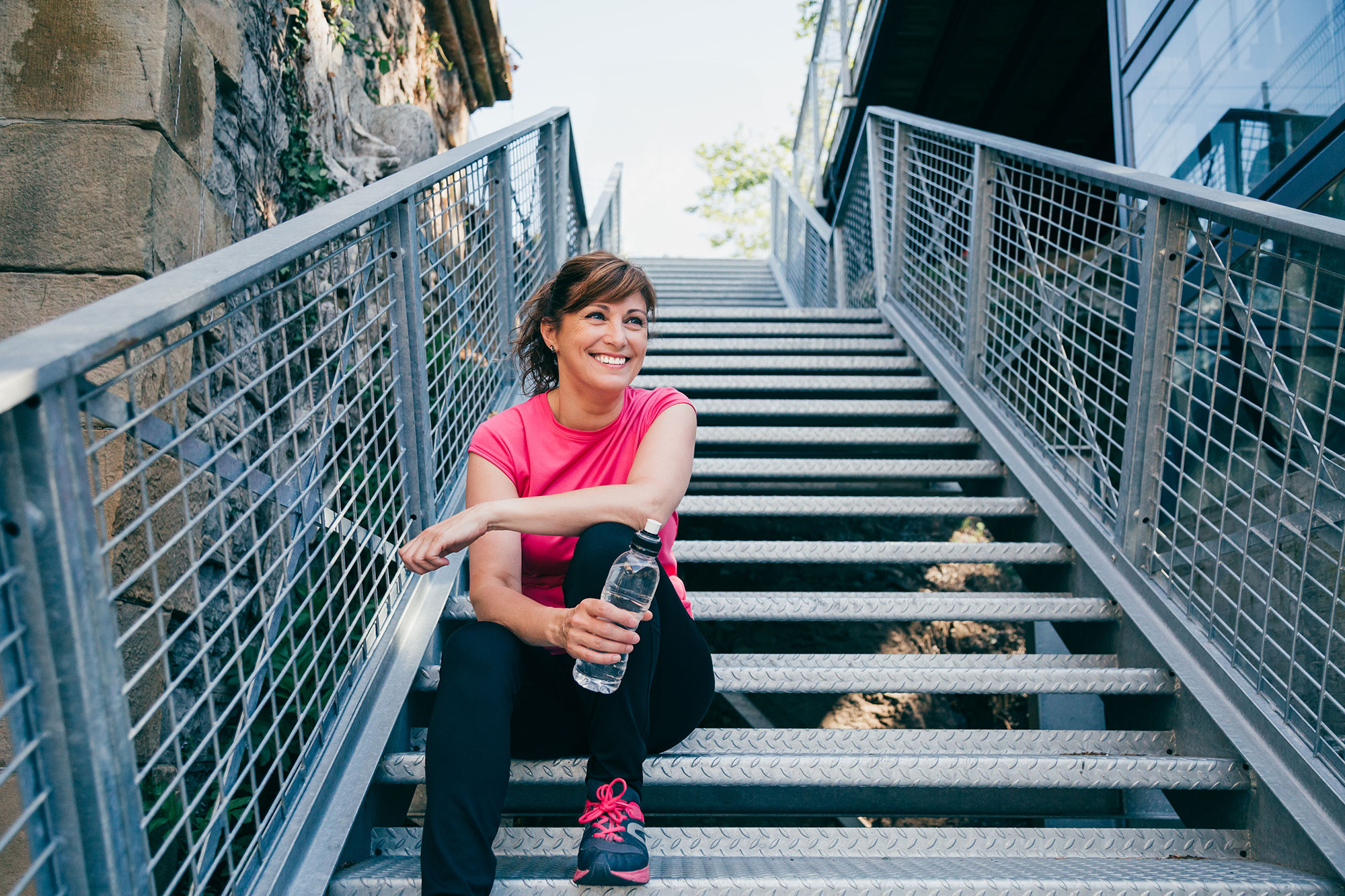Middle aged woman sits on steps outdoors holding water bottle