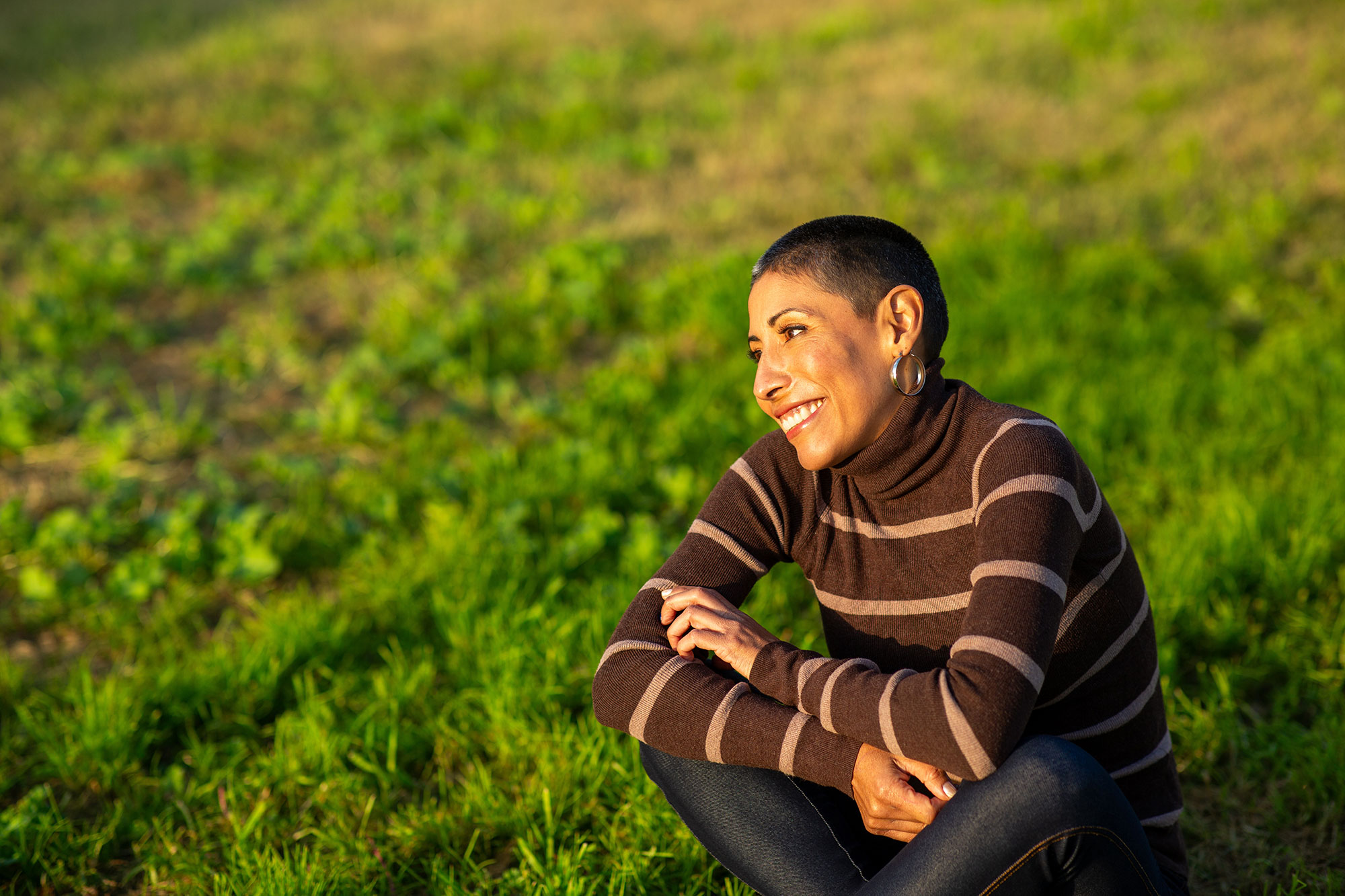 Middle aged woman smiles while sitting cross-legged in grass