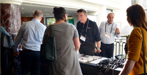 Group of four people stand around a laptop on a table and discuss what is on the screen.