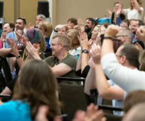 Large group of Tessitura team members applauding and cheering at an earlier in-person team meeting.