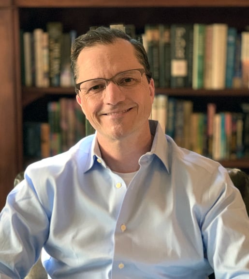 Andrew Recinos, seen from the torso up, seated in front of a bookcase.