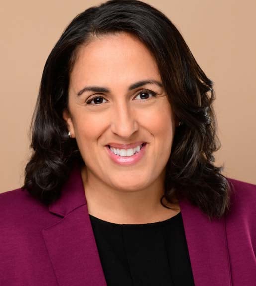 Headshot of a smiling woman with shoulder-length dark hair wearing a deep magenta blazer and black shirt.