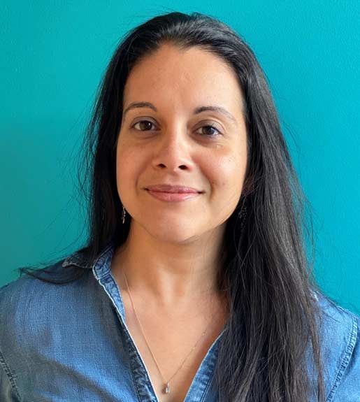 Photo of a woman with long dark hair, seen from the torso up, looking forward and smiling slightly.