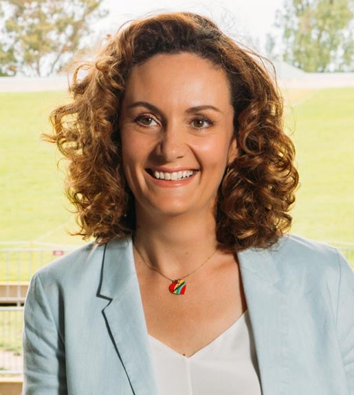 Claire Spencer, seen from the torso up, leaning on a rail with outdoor venue seating behind her.