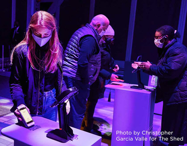 Woman scanning a contactless ticket in foreground with attendant assisting others in the background