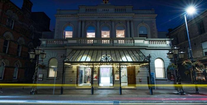 A stone building seen at night, with the blurred yellow light of a car having just gone by.