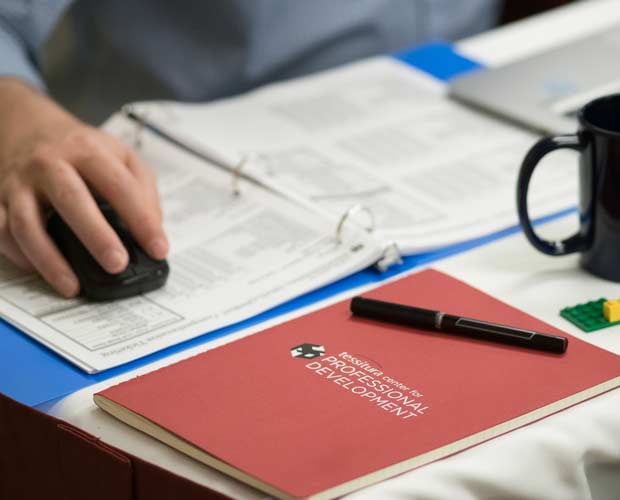 A notebook with "Tessitura Center for Professional Development" on the cover. Behind it, a person's hand on a wireless mouse