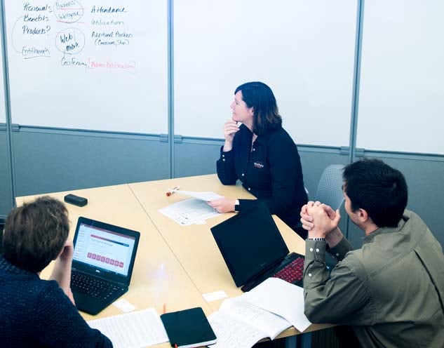 Three people sitting at a round table with laptops and papers