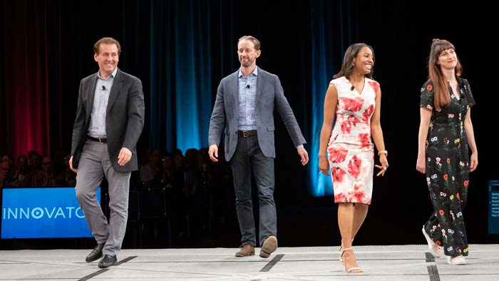 Four people stand on a stage, smiling and looking relaxed. 