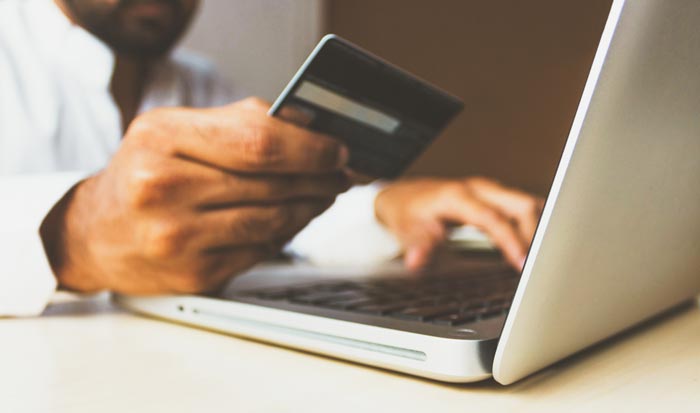 Close-up of a person's hands. One hand holds a credit card; the other hand is typing on a laptop.