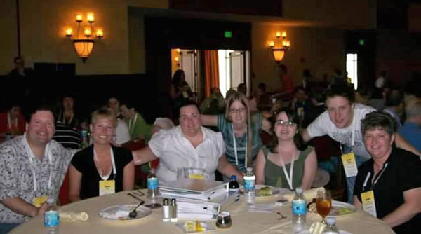 Several people are seated at a round table, facing forward and smiling. 