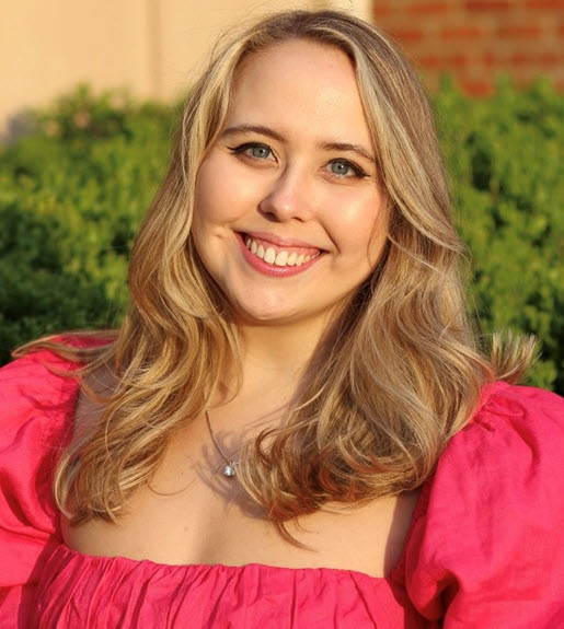 Photo of Katie Cullen, pictured outside and smiling towards the camera with long blond hair wearing a bright pink top.