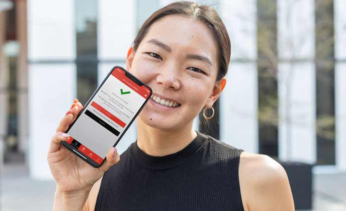 A woman, seen from the shoulders up, smiling holding up a cell phone showing a green checkmark and the words 'Thank you! You're all set.'