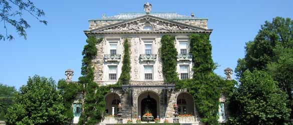 A large white house with ivy growing on it, surrounded by shrubbery, seen in daylight with a blue sky