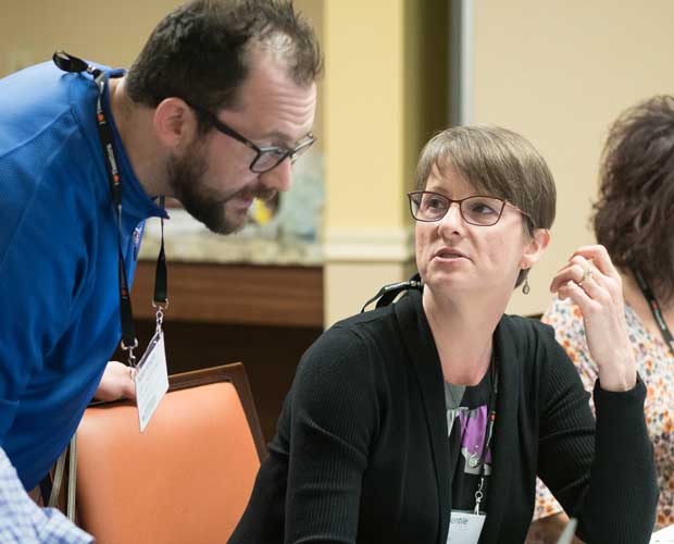 Gina Gentile, seated, looking up at a person standing nearby