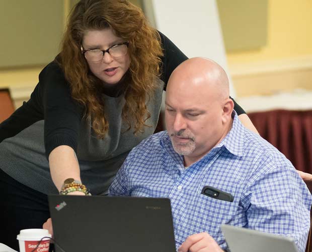 Tom Norcott, seated and looking at his laptop. An instructor is pointing at something on his screen.