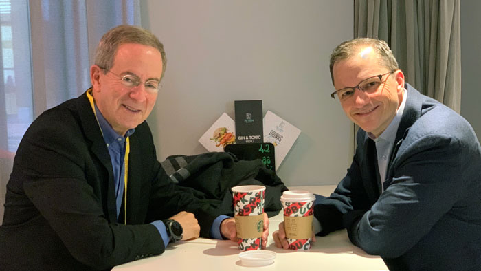 Jack Rubin at left, seated across from Andrew Recinos at right, each holding a paper coffee cup and facing out.