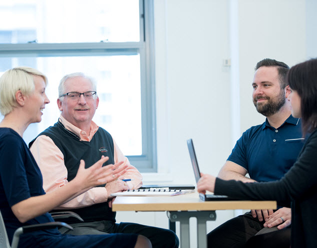 Four people sitting around a table with laptops and papers