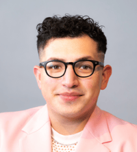 Headshot of Carlos Garcia Leon wearing a pink shirt and jacket with black glasses.