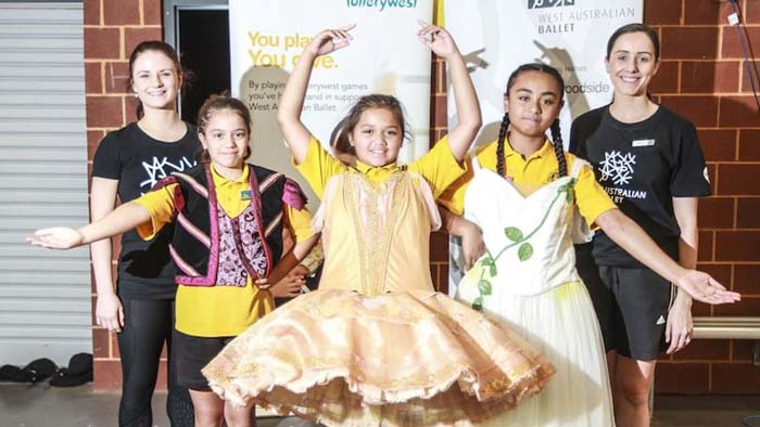 Three young students and two teaching artists pose for a photo. The students are wearing dance costumes, and the teaching artists are in black.
