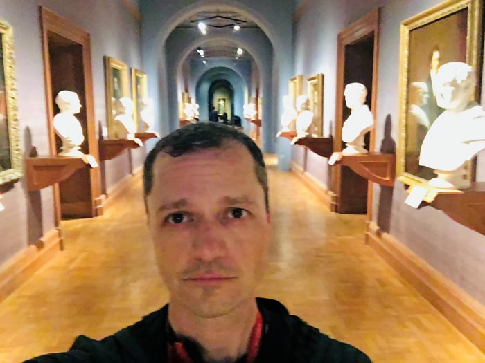 Selfie of Andrew with portraits and busts behind him