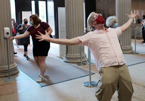 Man with arms outstretched at entrance to Met Museum wearing a red facemask.