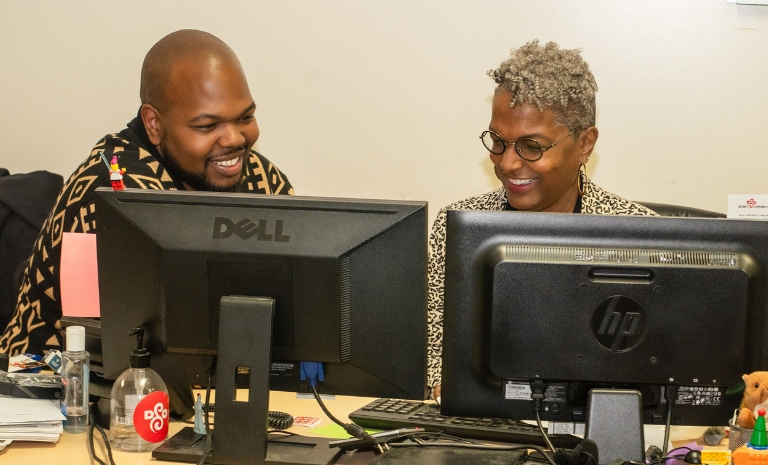 Evan and Sharon behind desktop computers working together.