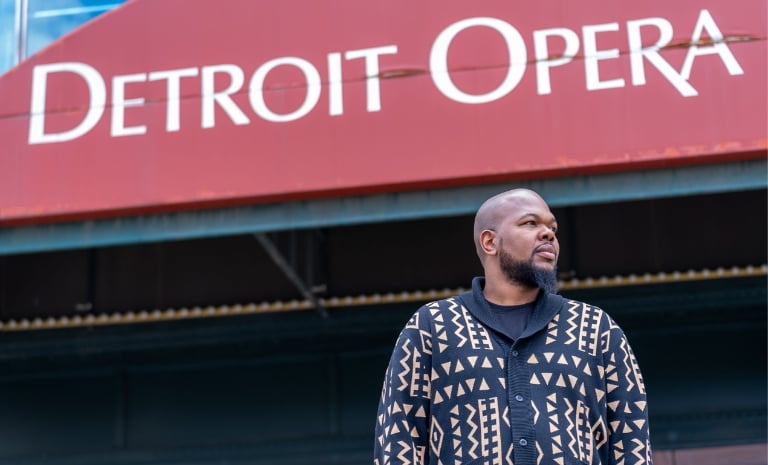 Evan stands outside building with Detroit Opera sign, looking to his left.