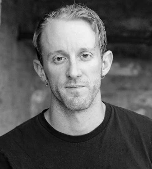 A black and white photo of Chris Plevin, seen from the shoulders up, wearing a dark t-shirt.