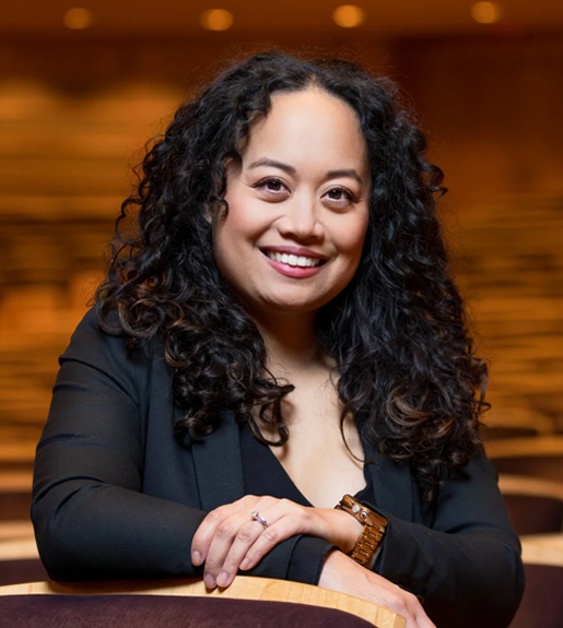 Imelda Tecson Juarez wears a black shirt and smiles in an auditorium.