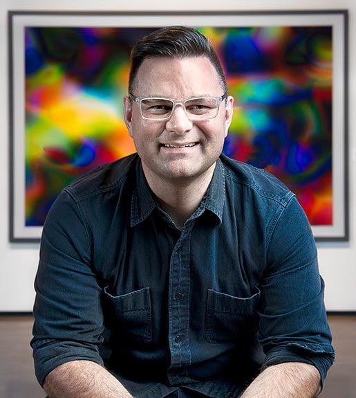 Scott Stulent, seated in front of a painting, seen from the waist up