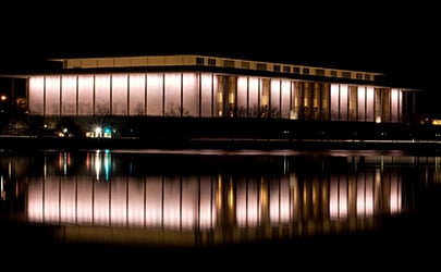 An exterior image of the Kennedy Center for the Performing Arts with the illuminated building reflected in the waters of the Potomac River.
