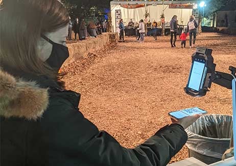 A person wearing a mask holding her phone underneath a barcode scanner mounted on a stand.