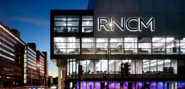A building at night with the windows lit up and the letters "RNCM" illuminated.