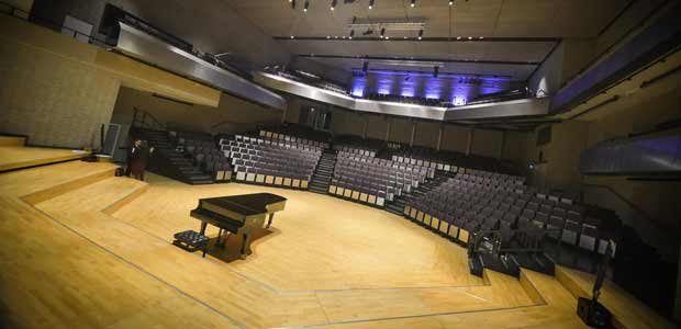 A wide shot of a concert hall. The stage, with a grand piano on it, is in the foreground, with the seats behind.