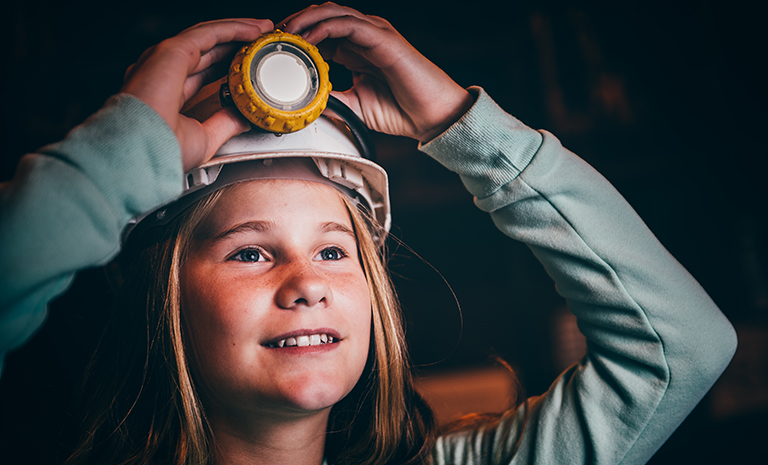 A young visitor wearing a hard hat with a light explores the underground mine at the Big Pit National Coal Museum in Wales.