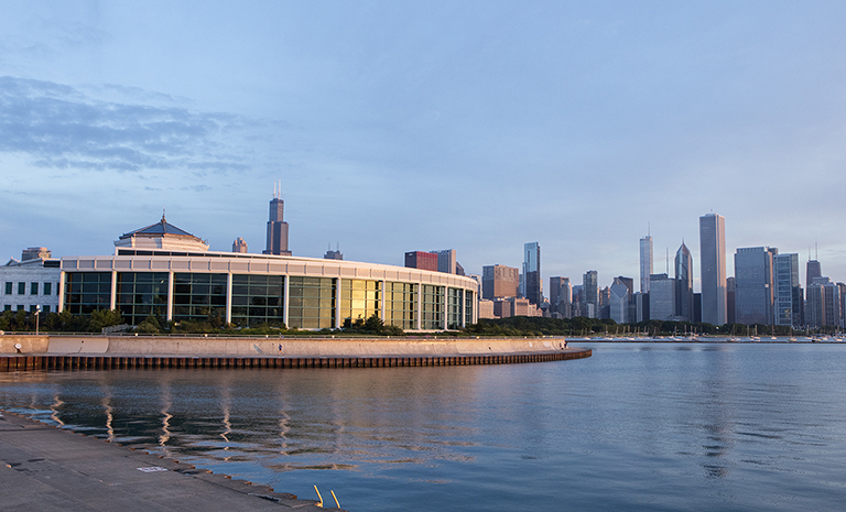 The exterior of Shedd Aquarium on the banks of Lake Michigan with the Chicago skyline in the background.