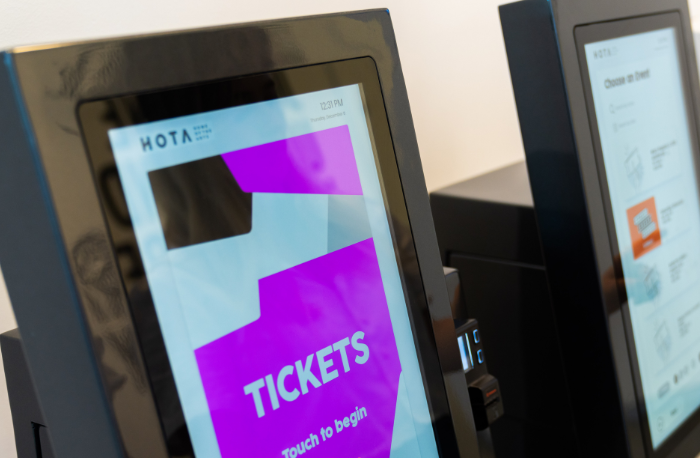 Person standing at kiosk with the screen reading 'Tickets - touch to begin'