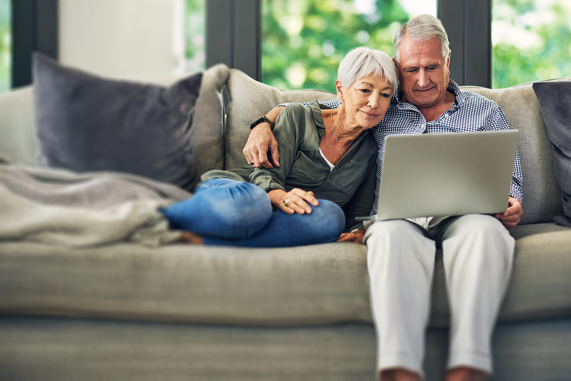 Older couple sitting on a couch together looking at a laptop screen.