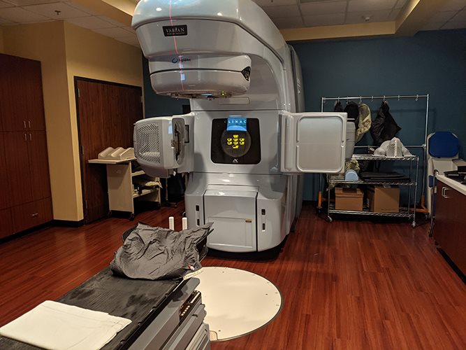 Varian linear accelerator with visible positioning laser and patient couch in a radiation therapy treatment room