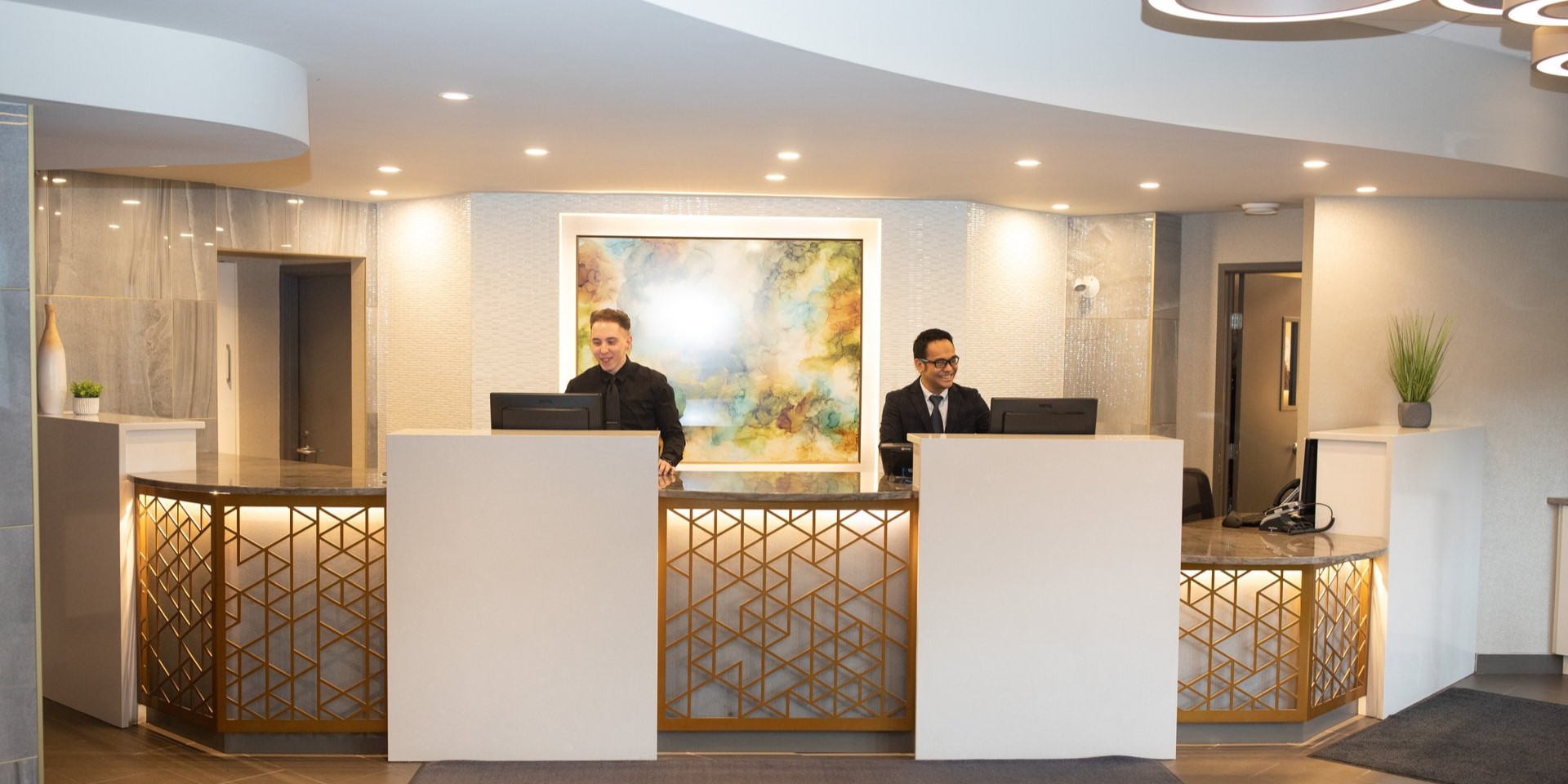 Two men standing behind a counter topped by computer terminals at a hotel front desk