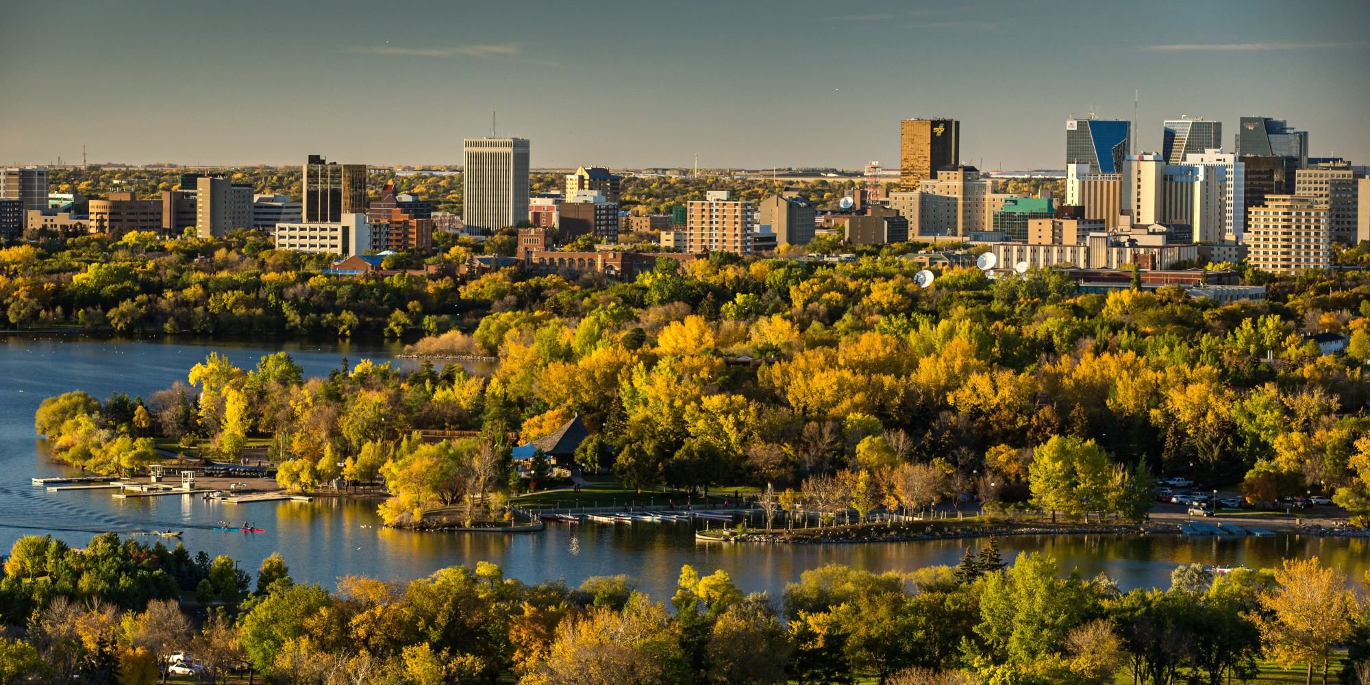 Oblique arial view of a city skyline behind a body of water under a clear sunny sky with green and golden foliage on trees in early autumn